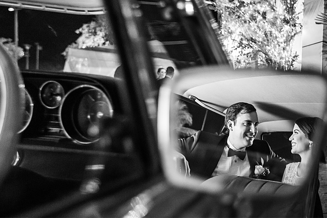 Newlyweds smiling at one another in the reflection of a classic car mirror