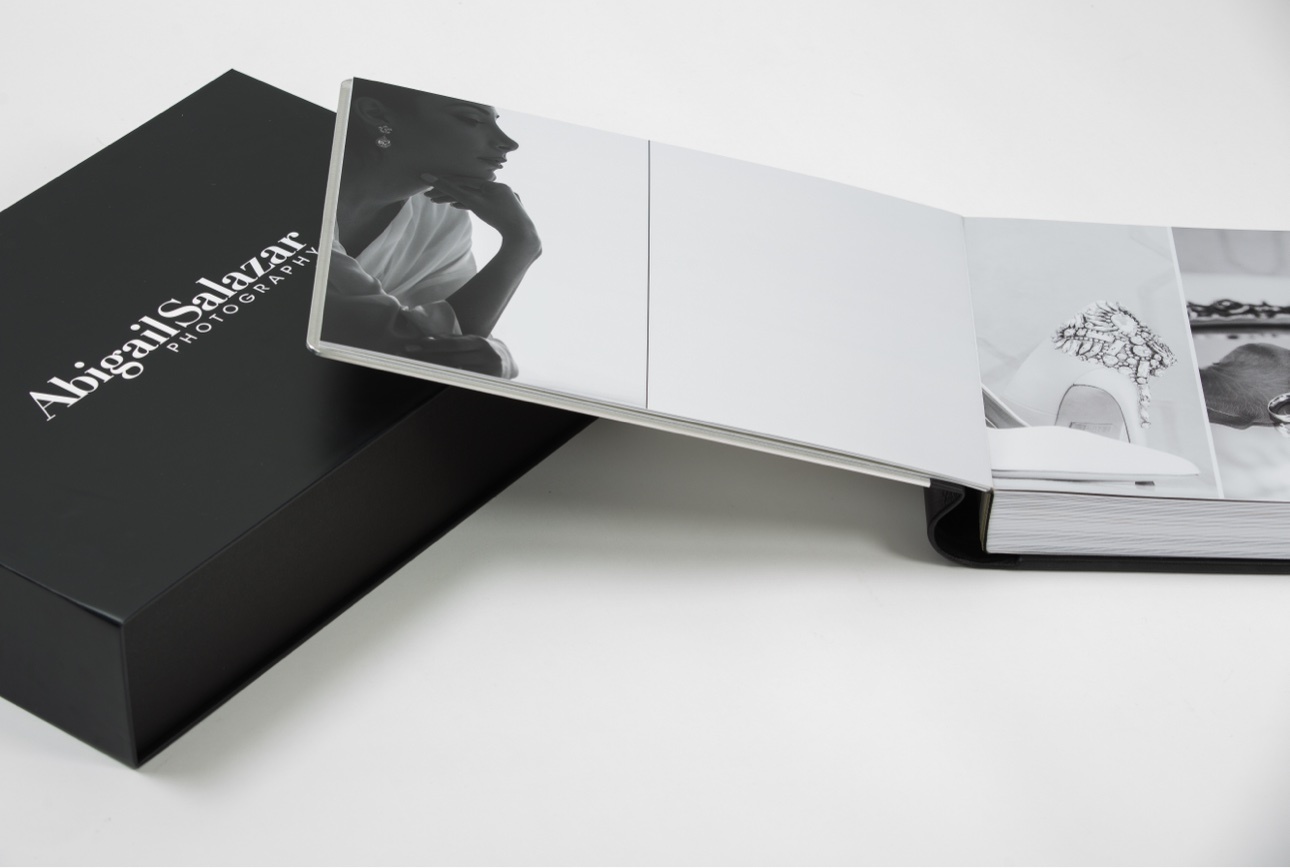 Open fine-art wedding album displayed beside a black Abigail Salazar Photography presentation box