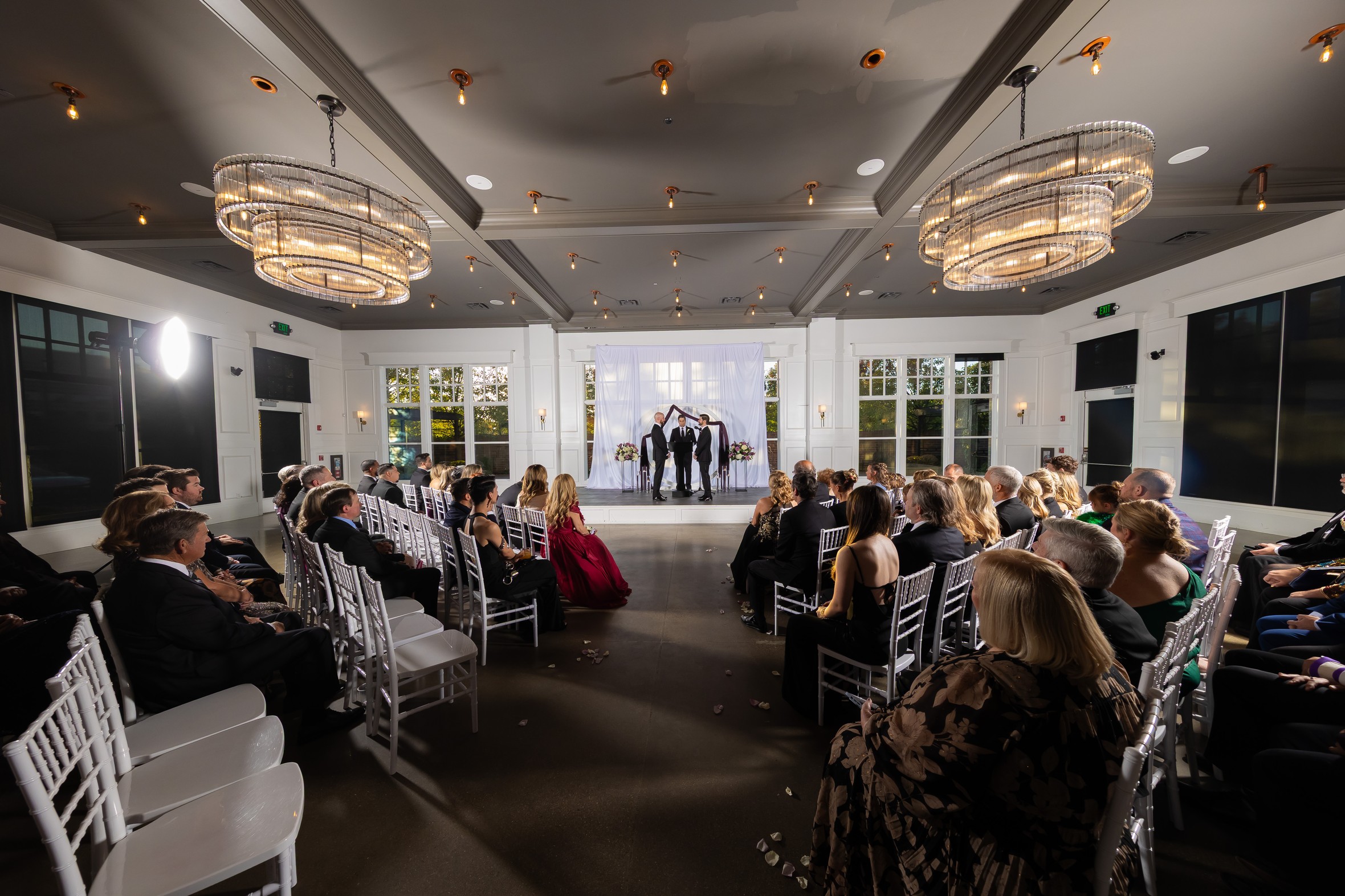 The wedding ceremony at The Crawford, guests seated on white chairs facing the couple beneath crystal chandeliers