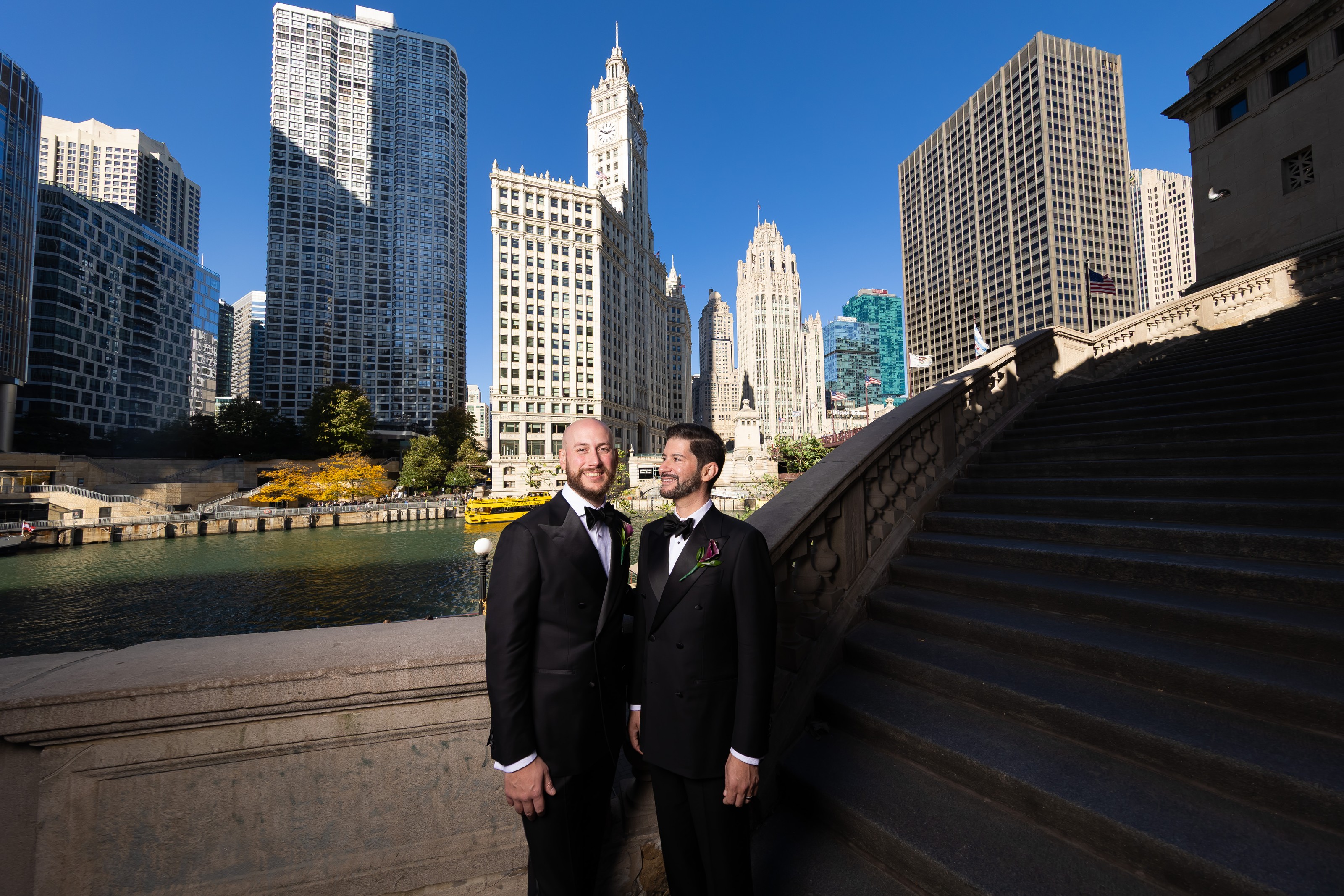 Michael and Kevin in black tie on the Chicago Riverwalk, the Wrigley Building clock tower rising behind them