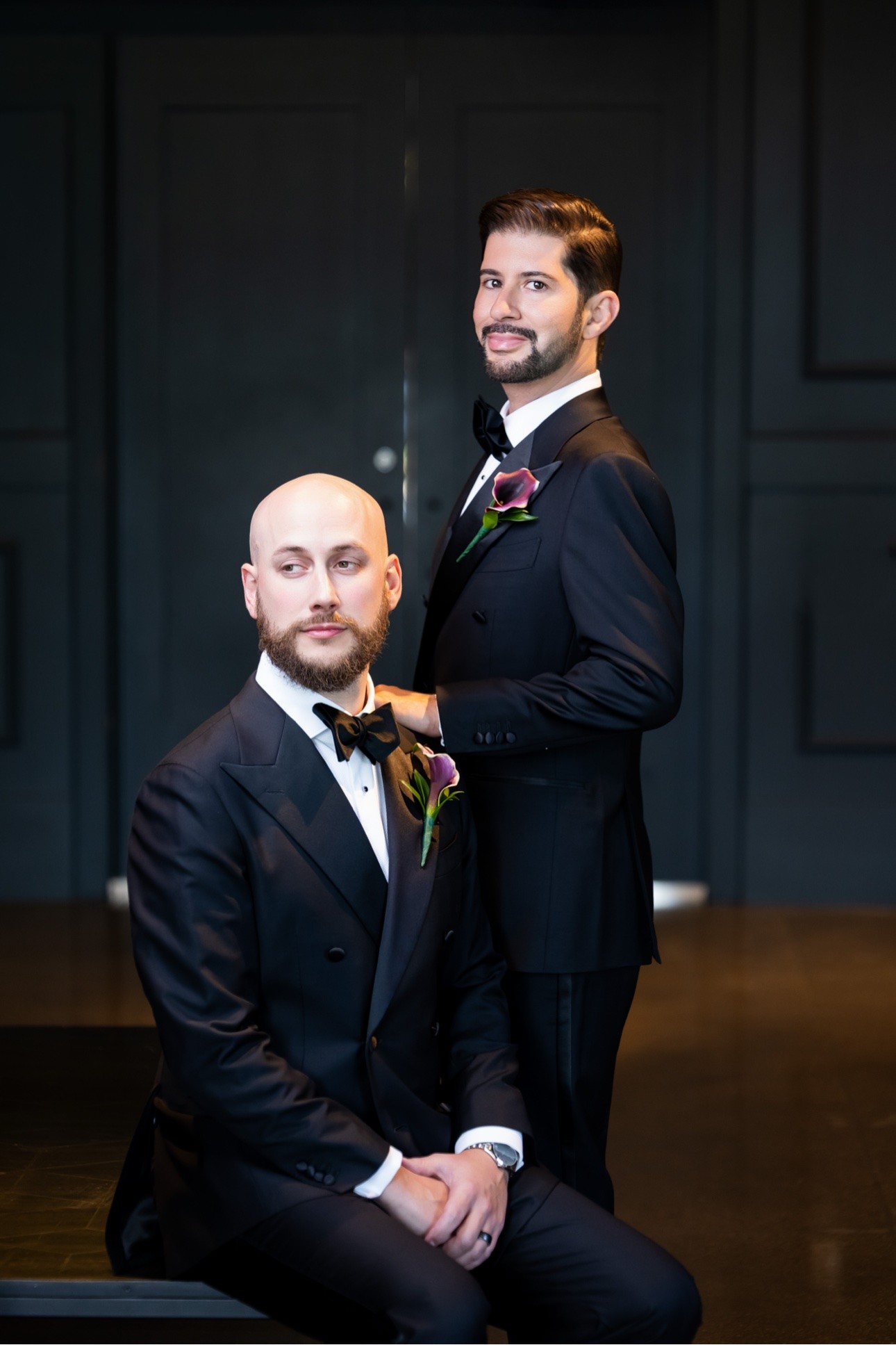 Michael and Kevin in black tie sharing a formal wedding portrait against dark paneled doors